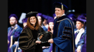 Paul Farrell is presented an award while wearing full academic regalia